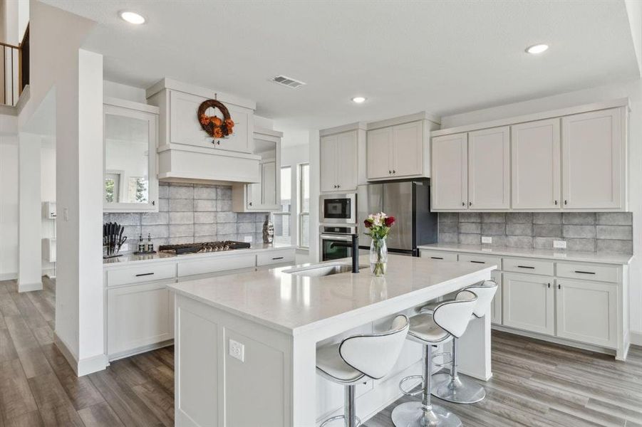Kitchen with a breakfast bar area, light stone countertops, stainless steel appliances, light wood-style floors, and a kitchen island with sink Kitchen with a breakfast bar area, light stone countertops, stainless steel appliances, light wood-style floors, and a kitchen island with sink