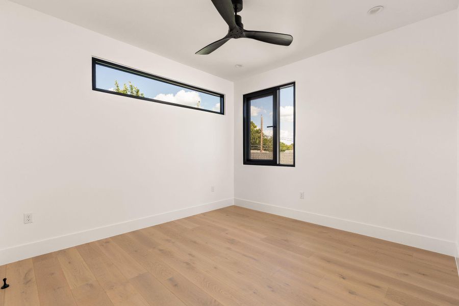 Blonde hardwood floors complement bright white walls and a sleek ceiling fan in this versatile room.
