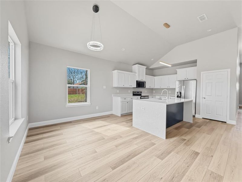 Kitchen featuring white cabinets, an island with sink, light wood-type flooring, hanging light fixtures, and vaulted ceiling