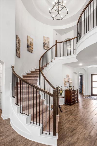 Staircase featuring arched walkways, wood finished floors, a raised ceiling, a chandelier, and a high ceiling Staircase featuring arched walkways, wood finished floors, a raised ceiling, a chandelier, and a high ceiling