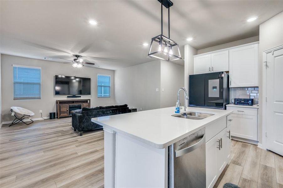 Kitchen featuring white cabinetry, hanging light fixtures, freestanding refrigerator, dishwasher, and decorative backsplash