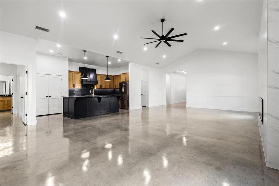 Unfurnished living room featuring concrete flooring, a ceiling fan, vaulted ceiling, and recessed lighting