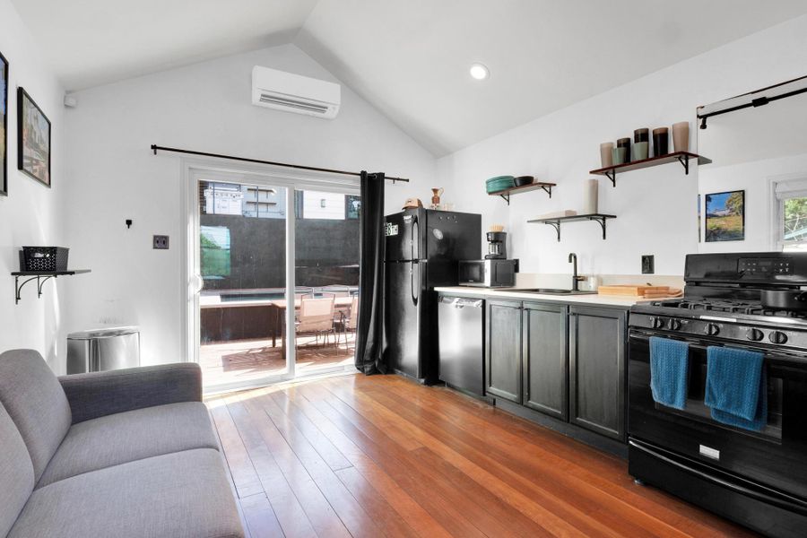 Kitchen with black appliances, open shelves, a wall mounted AC, healthy amount of natural light, and lofted ceiling