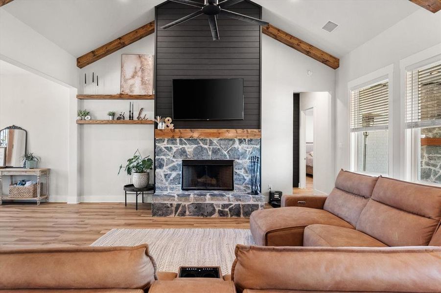 Living room with wood finished floors, a stone fireplace, and a ceiling fan