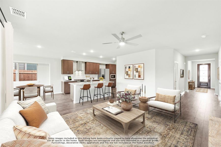 Open-concept living room with hardwood floors and ceiling fan, flowing into kitchen with dark wood cabinets and island seating