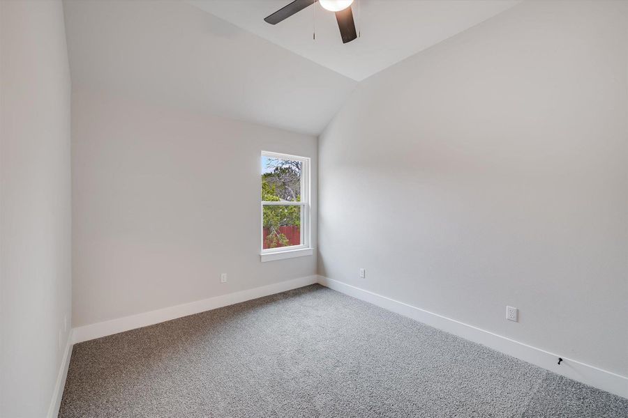 Unfurnished room featuring ceiling fan, carpet, baseboards, and vaulted ceiling