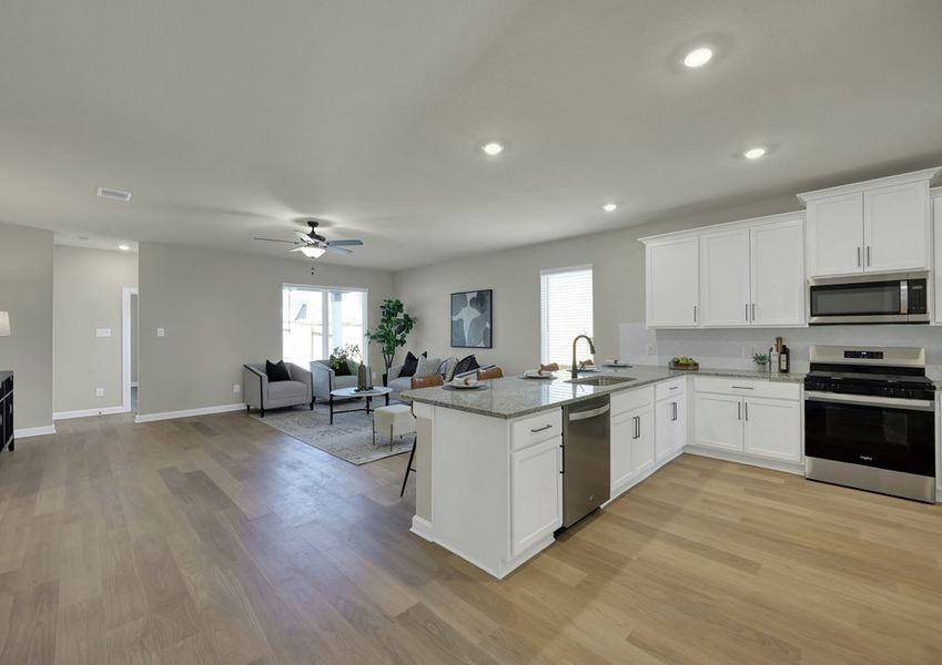 Wide view of the open-concept kitchen and living space with white cabinetry, granite countertops, and stainless steel appliances.