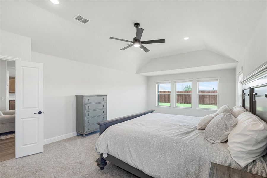 Spacious bedroom with vaulted ceiling, ceiling fan, carpet flooring, and large window with backyard view