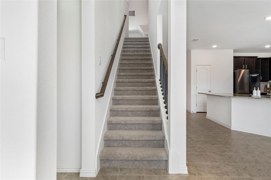 A grand carpeted staircase leads to the upper level, complementing the tiled flooring and offering views of the adjoining kitchen. A grand carpeted staircase leads to the upper level, complementing the tiled flooring and offering views of the adjoining kitchen.