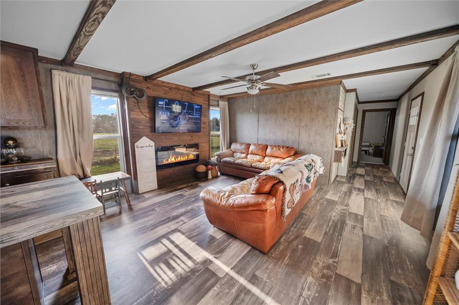 Living area featuring wooden walls, wood finished floors, a fireplace, beamed ceiling, and ceiling fan Living area featuring wooden walls, wood finished floors, a fireplace, beamed ceiling, and ceiling fan
