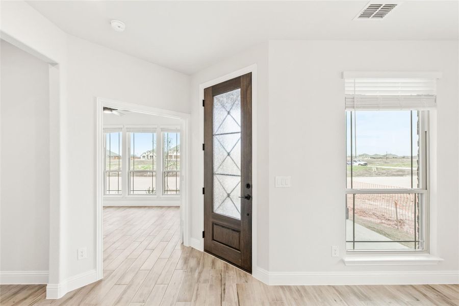 Bright entryway with dark wood front door featuring glass panels and light hardwood floors Bright entryway with dark wood front door featuring glass panels and light hardwood floors