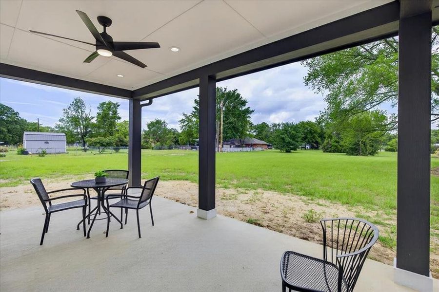 Spacious covered patio with a concrete surface, featuring a modern ceiling fan with integrated lighting
