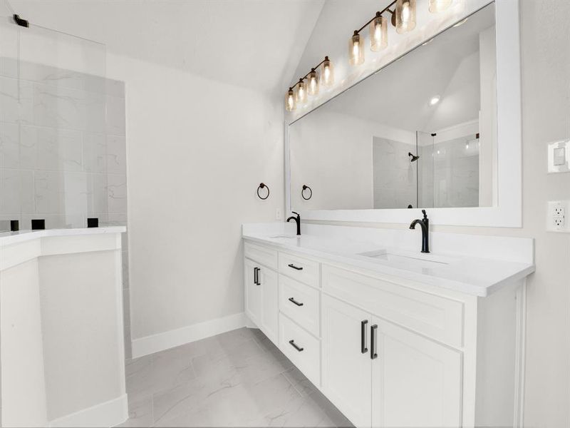 Bathroom featuring a marble finish shower, double vanity, lofted ceiling, and light marble finish flooring