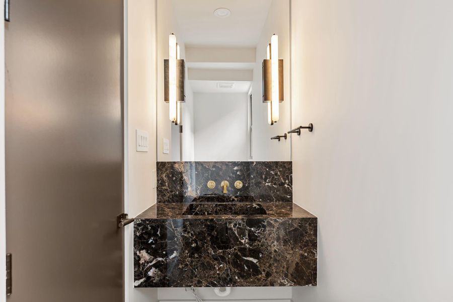 Stepping into the powder tucked off the entry, a marble Fior di Bosco vanity, marble sconces, and espresso door anchor the space.