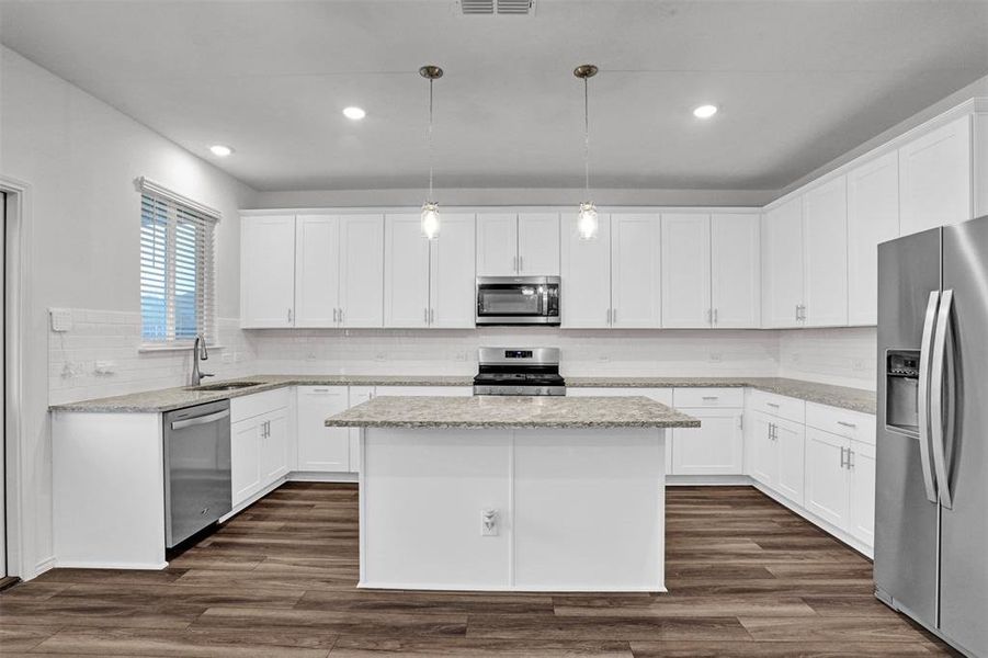 Spacious kitchen featuring white cabinetry, stone countertops, stainless steel appliances, a central island, and wood-finish flooring