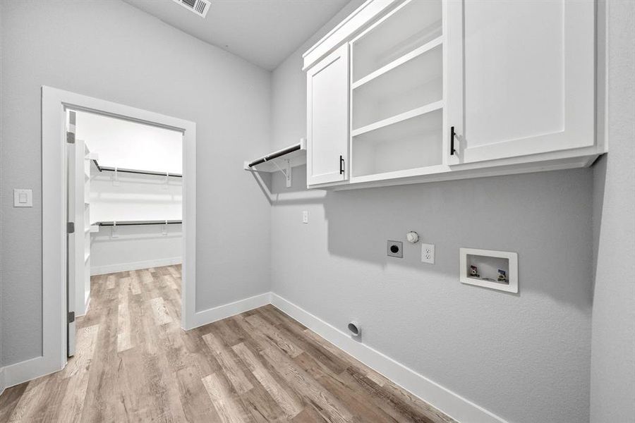 Washroom with light wood finished floors, cabinet space, hookup for a washing machine, hookup for an electric dryer, and hookup for a gas dryer