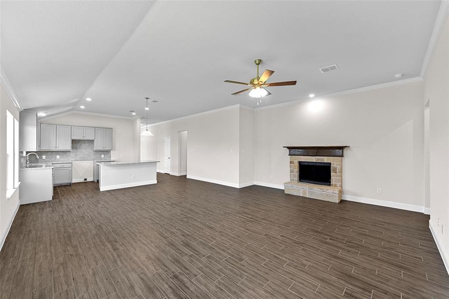 Unfurnished living room featuring ceiling fan, ornamental molding, dark wood-type flooring, a stone fireplace, and sink