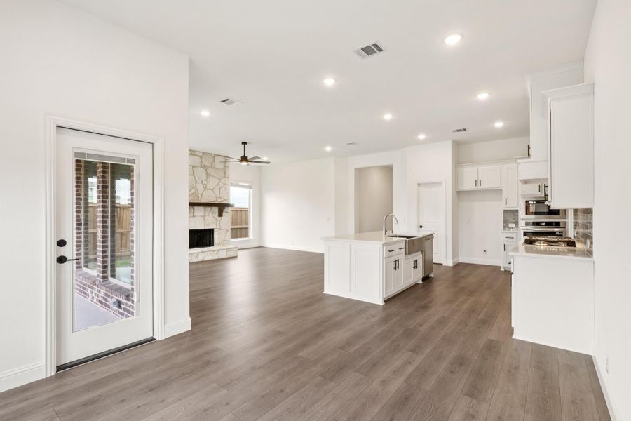 Open-concept kitchen and living area with white cabinets, center island, hardwood floors, and stone fireplace