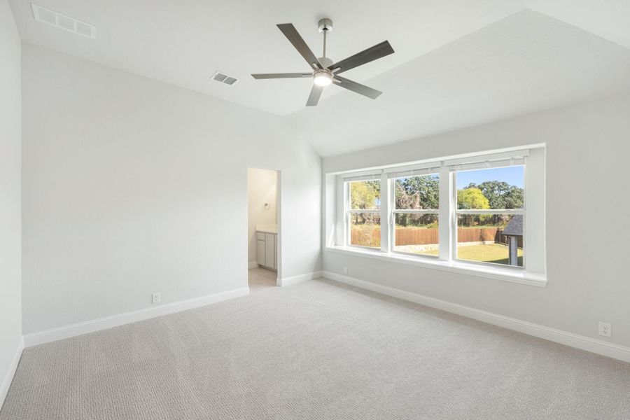 Empty bedroom with vaulted ceiling, ceiling fan, carpet, and large windows overlooking backyard
