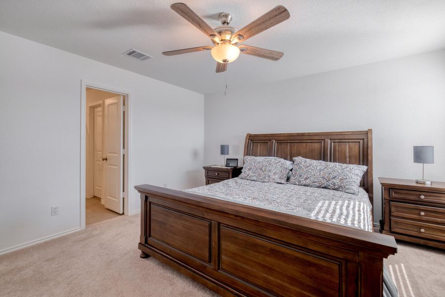 This bedroom features neutral-toned carpet, white walls, and a ceiling fan with an integrated light fixture
