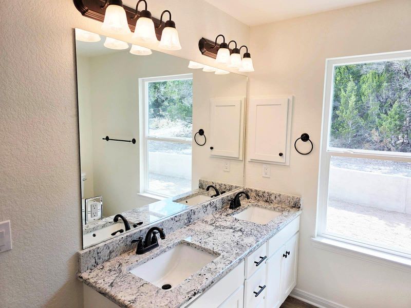 Bathroom featuring a textured wall, double vanity, and plenty of natural light