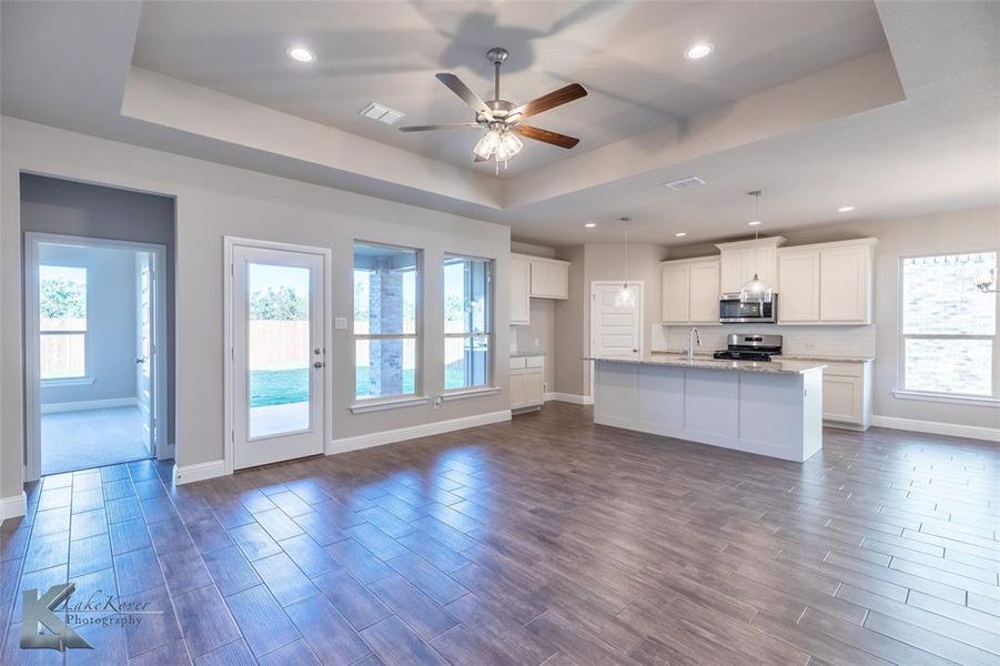 Unfurnished living room featuring a tray ceiling, healthy amount of natural light, dark wood finish ceramic tile floors, recessed lighting, and a ceiling fan