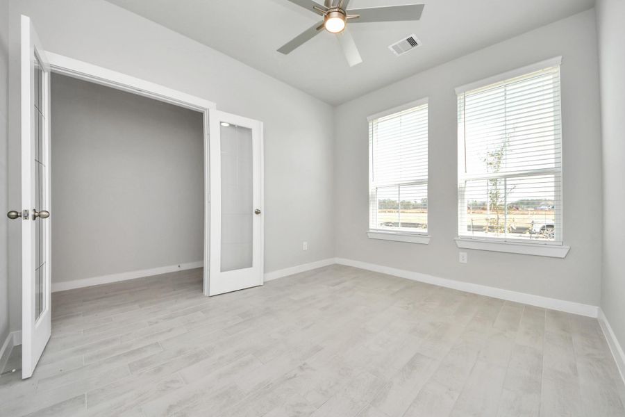 Experience the perfect blend of sophistication and warmth in this home office, boasting elegant wood-look tile flooring and flooded with natural light from expansive windows and French doors. Sample photo of completed home with similar floor plan. Actual colors and selections may vary.