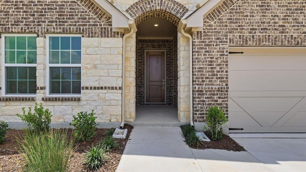 Brick and stone facade featuring an arched entryway and a panel-style garage door Brick and stone facade featuring an arched entryway and a panel-style garage door