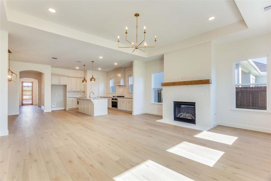 Unfurnished living room with a raised ceiling, light hardwood / wood-style flooring, and a chandelier