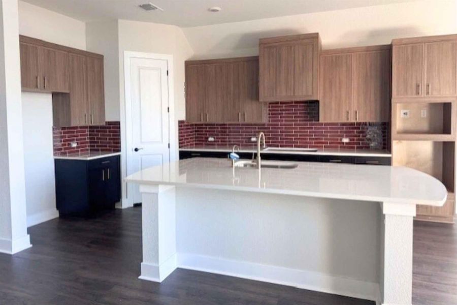Kitchen with a kitchen island with sink, a kitchen breakfast bar, dark wood finished floors, light stone countertops, and decorative backsplash