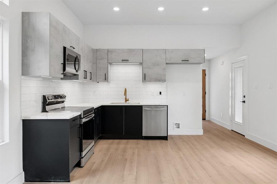 Kitchen with stainless steel appliances, light wood finished floors, decorative backsplash, light countertops, and recessed lighting