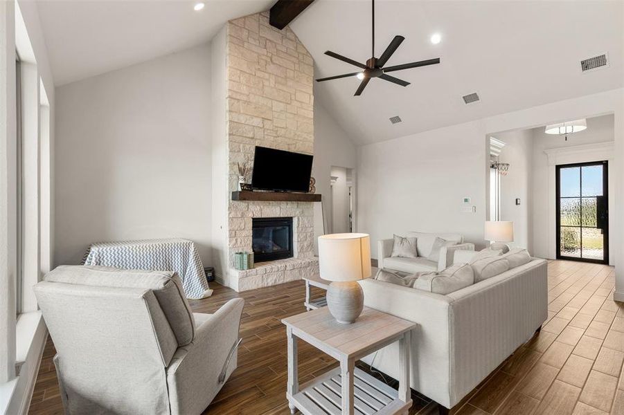 Living area featuring beamed ceiling, visible vents, a ceiling fan, a fireplace, and wood tiled floor