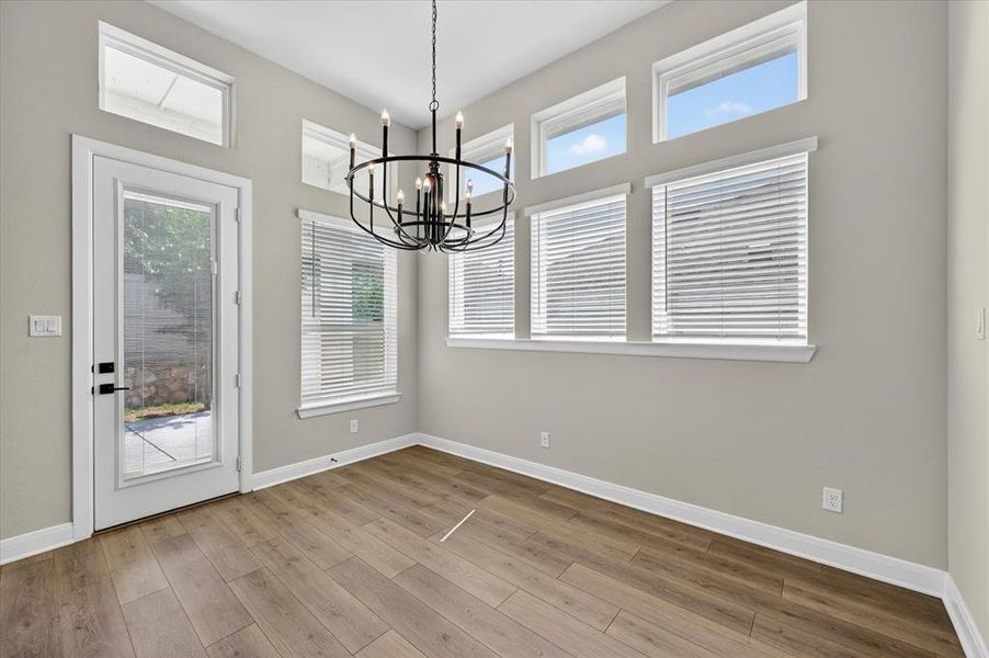 Spacious room featuring vaulted ceilings, wood-finish flooring, a full-light door, and an overhead chandelier Spacious room featuring vaulted ceilings, wood-finish flooring, a full-light door, and an overhead chandelier