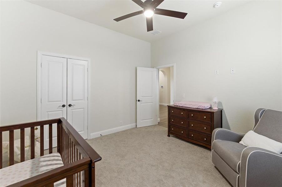 Bedroom with a nursery area, a closet, light carpet, and a ceiling fan
