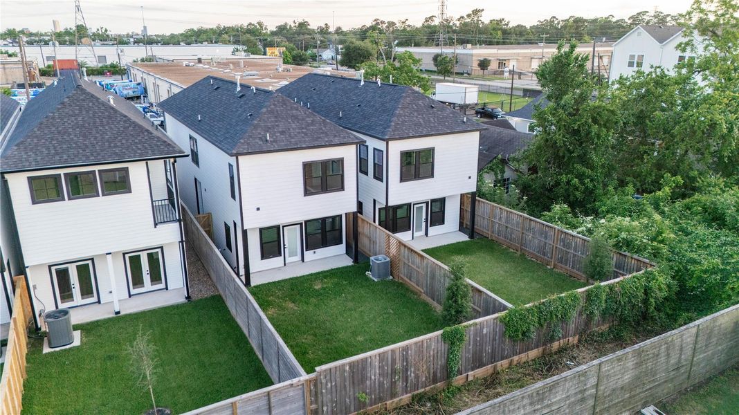 This aerial view shows a modern, two-story home with sleek, dark roofs and white exteriors. Each home has a fenced, spacious, and private backyard.