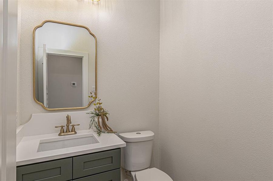 Powder room featuring a sage green vanity with white countertop, integrated sink, and brass-finish fixtures