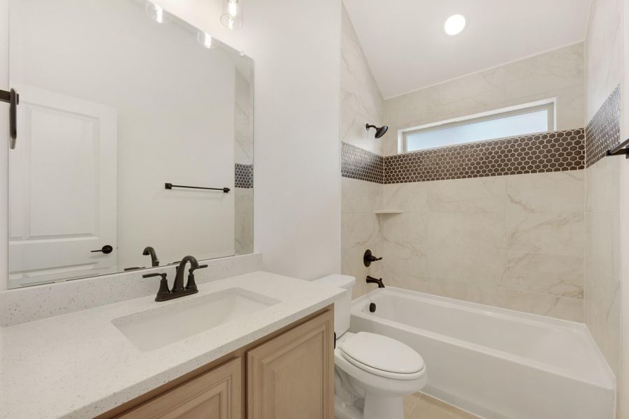 Bathroom with quartz vanity, tub-shower combo with marble tile, and dark bronze fixtures