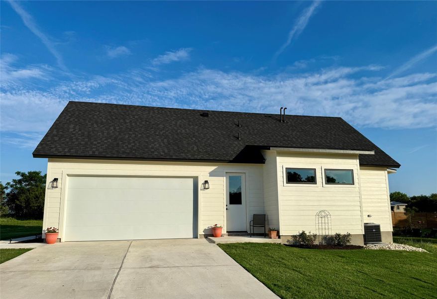 View of front of home with central AC unit, driveway, a front lawn, a garage, and a shingled roof