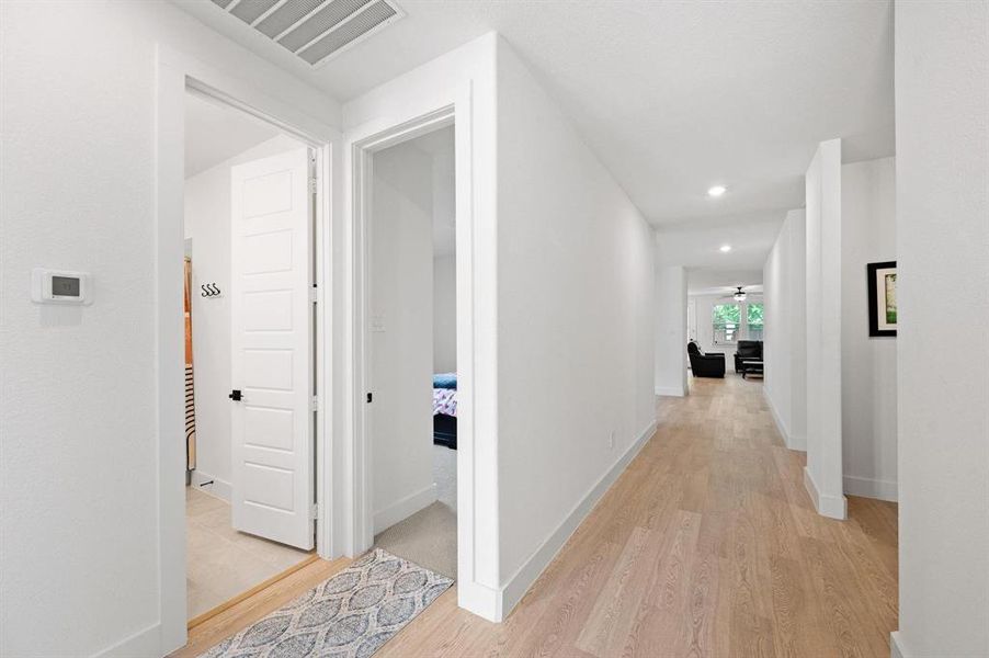 Hallway with light wood-finish flooring extending into living spaces, white walls, and recessed lighting Hallway with light wood-finish flooring extending into living spaces, white walls, and recessed lighting