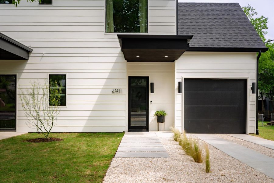 View of exterior entry with driveway, roof with shingles, and a garage