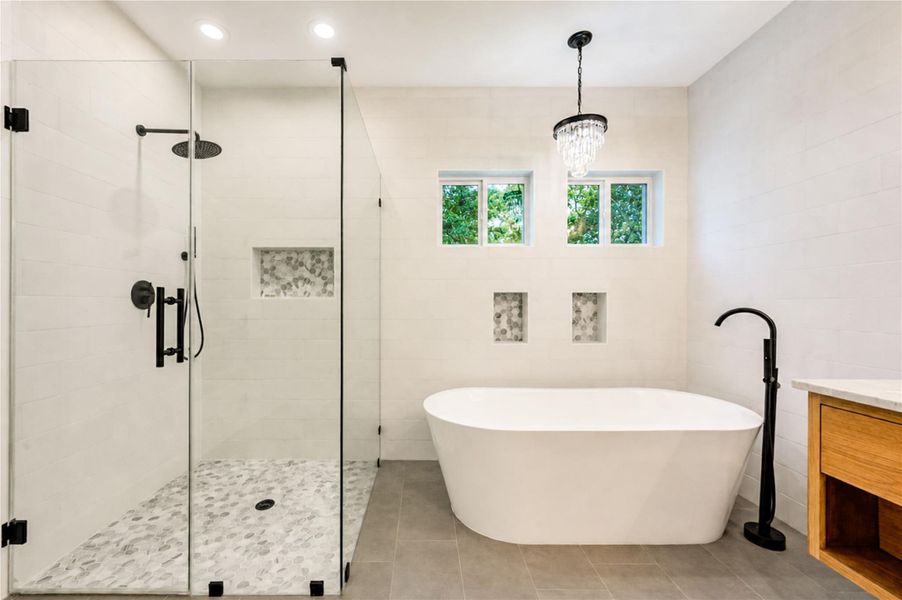 Luxurious Primary bathroom featuring a spacious glass-enclosed shower, elegant freestanding tub, and modern fixtures, all enhanced by natural light from stylish windows.