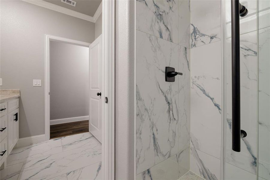 Full bath featuring vanity, ornamental molding, a marble finish shower, visible vents, and baseboards Full bath featuring vanity, ornamental molding, a marble finish shower, visible vents, and baseboards