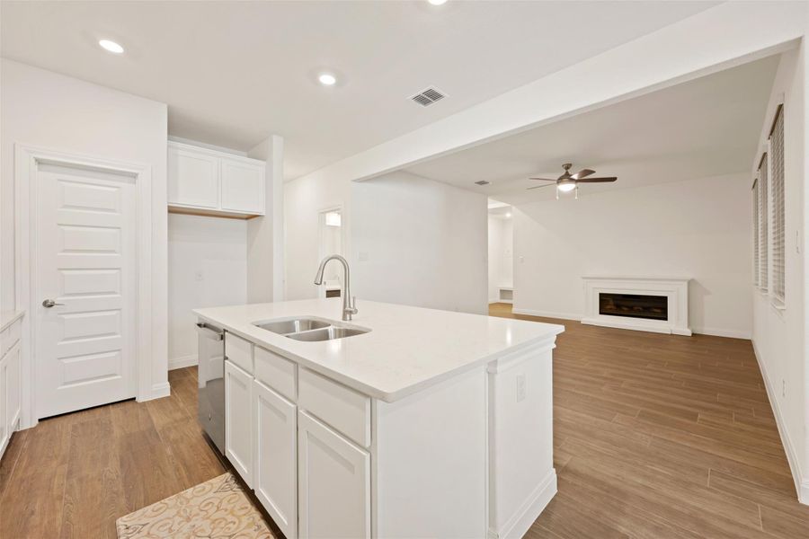 Kitchen with white cabinets, light wood-style floors, a fireplace, ceiling fan, and open floor plan Kitchen with white cabinets, light wood-style floors, a fireplace, ceiling fan, and open floor plan