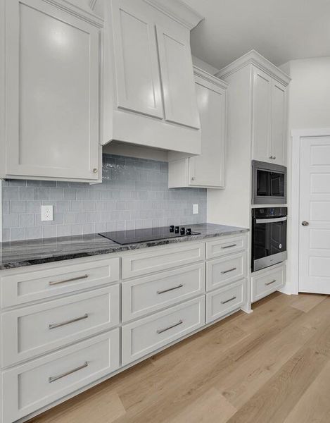 Kitchen with dark stone counters, white cabinetry, wall oven, and tasteful backsplash