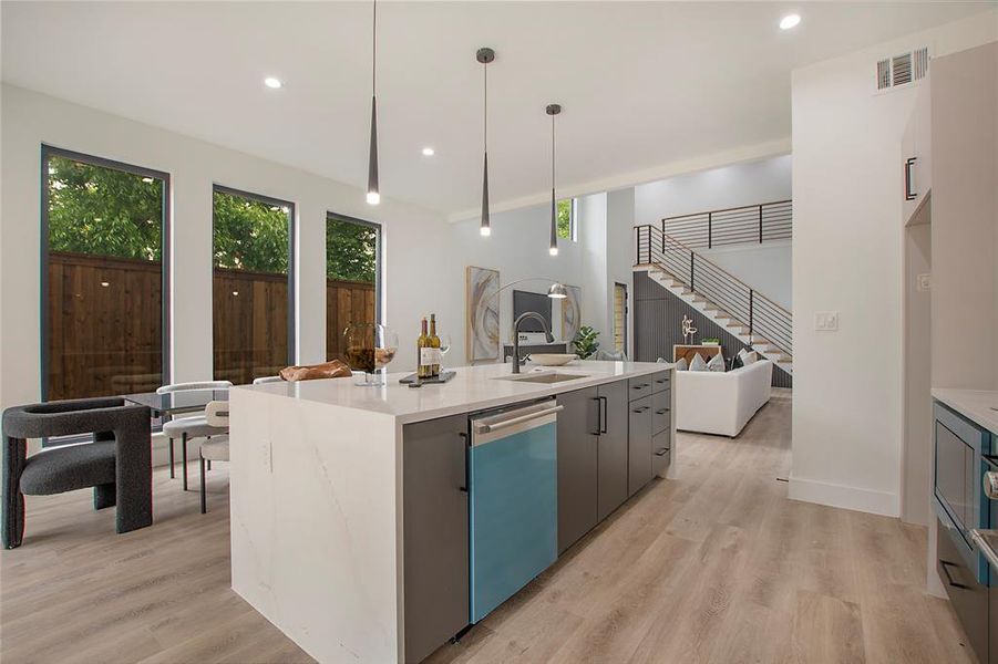 Kitchen featuring an island with sink, sink, hanging light fixtures, stainless steel dishwasher, and light hardwood / wood-style floors