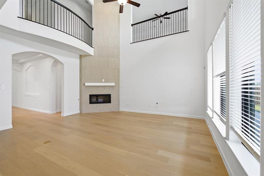 Spacious living area featuring high ceilings, wood-finish flooring, and a floor-to-ceiling fireplace with a mantel Spacious living area featuring high ceilings, wood-finish flooring, and a floor-to-ceiling fireplace with a mantel