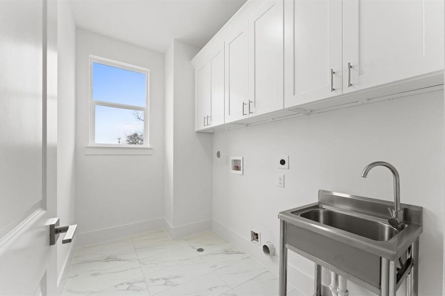 This photo shows a bright, modern laundry room featuring sleek white cabinetry, a stainless steel utility sink, and a tiled floor. A window allows natural light to fill the space, creating a clean and functional area for laundry tasks.