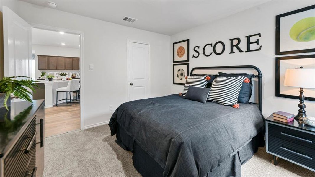 Spacious room featuring neutral carpeting, a white interior door, and a doorway opening to a kitchen with wood-finish flooring, white countertops, and dark wood cabinetry Spacious room featuring neutral carpeting, a white interior door, and a doorway opening to a kitchen with wood-finish flooring, white countertops, and dark wood cabinetry