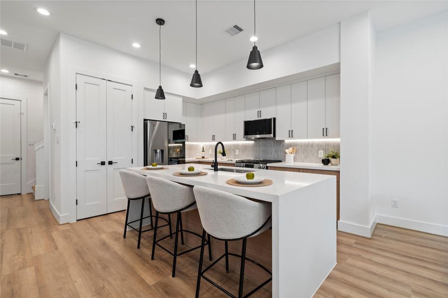 The heart of the home features a generous island with seating for 3-4, perfect for casual conversations while cooking. Matte black fixtures and soft under-cabinet lighting highlight the timeless mix of crisp white cabinetry and natural textures.