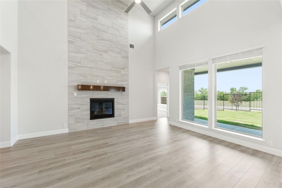 Open living room with vaulted ceiling, floor-to-ceiling tiled fireplace, wood mantel, and large windows overlooking backyard Open living room with vaulted ceiling, floor-to-ceiling tiled fireplace, wood mantel, and large windows overlooking backyard